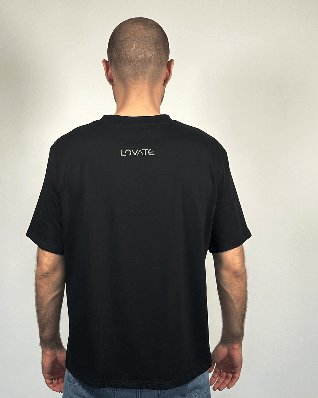 Овърсайз черна тениска, показана в гръб върху мъж, лого Lovate в центъра