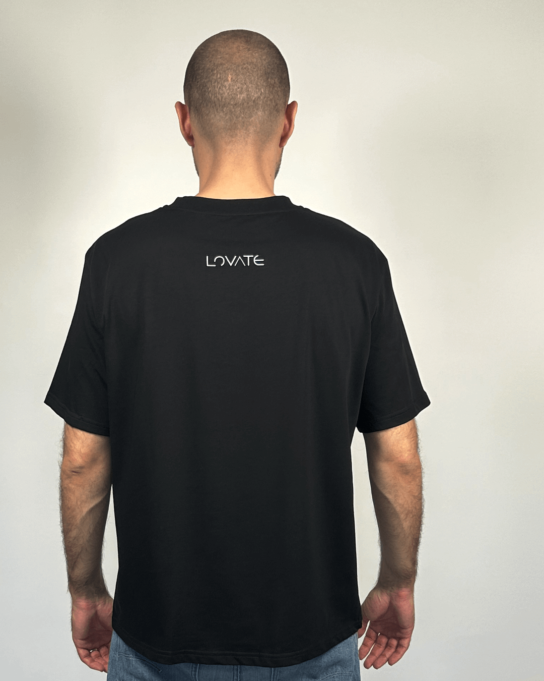 Овърсайз черна тениска, показана в гръб върху мъж, лого Lovate в центъра